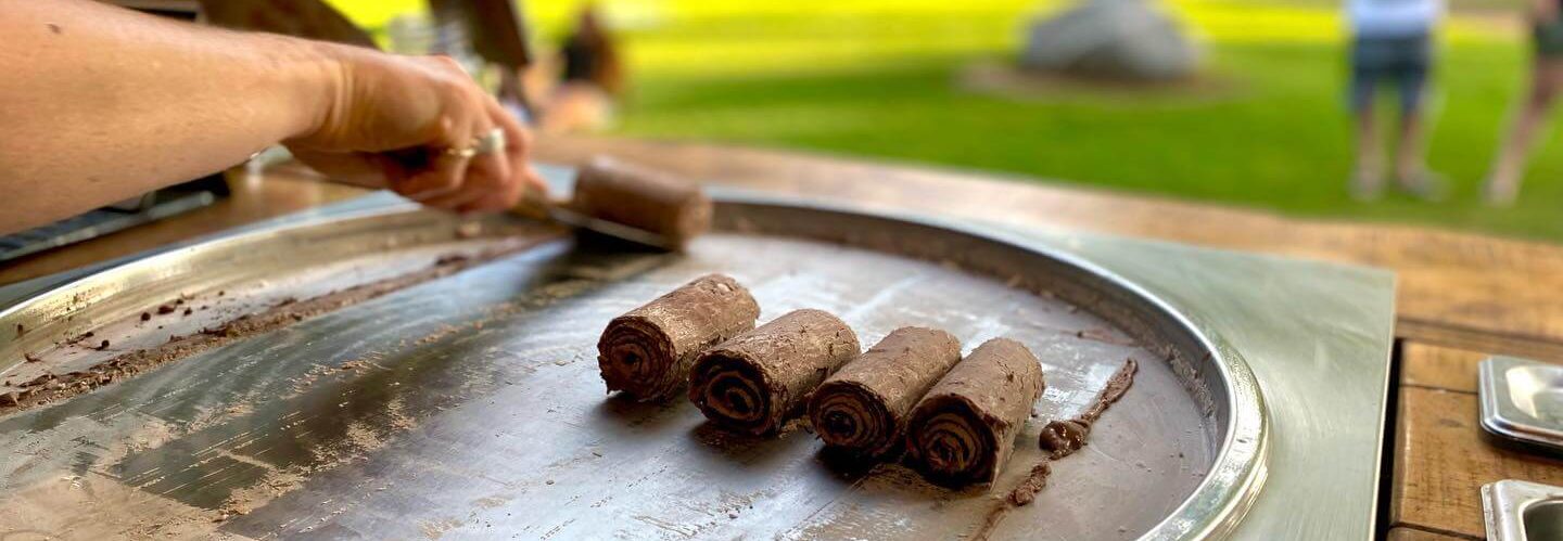 Four finished chocolate ice cream rolls standing on the frozen steel plate