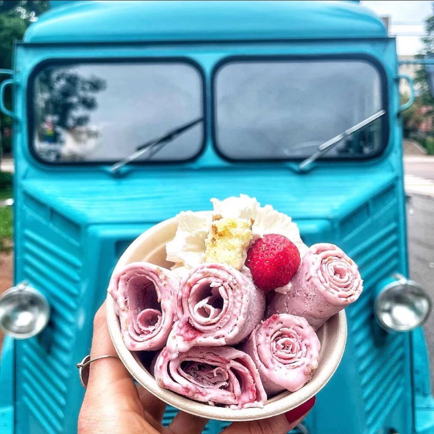 A cup of strawberry rolled ice cream held up in front of the blue truck